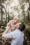 A baby girl holds her daddy's face as he hoists her above him