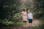 A brother and sister hold hands amongst the greenery on a dirt track
