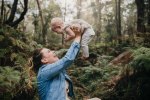 A mother laughs with her baby in a lush green forest